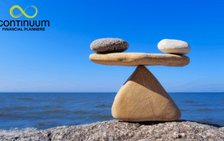 stones balanced on a rock fulcrum with a clear blue sky and a calm blue sea background reflective of investor risk profiling in action