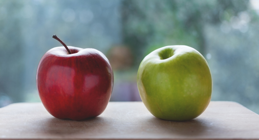 one red apple beside a green apple on a board and with a blurred background