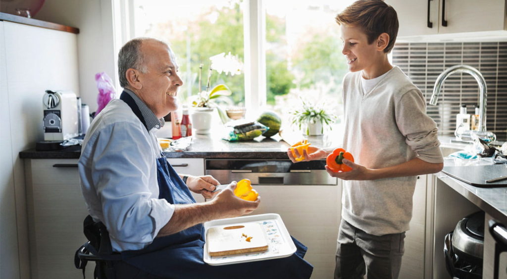 man-in-wheel-chair-peeling-vegetables-in-a-kitchen-with-a-young-boy